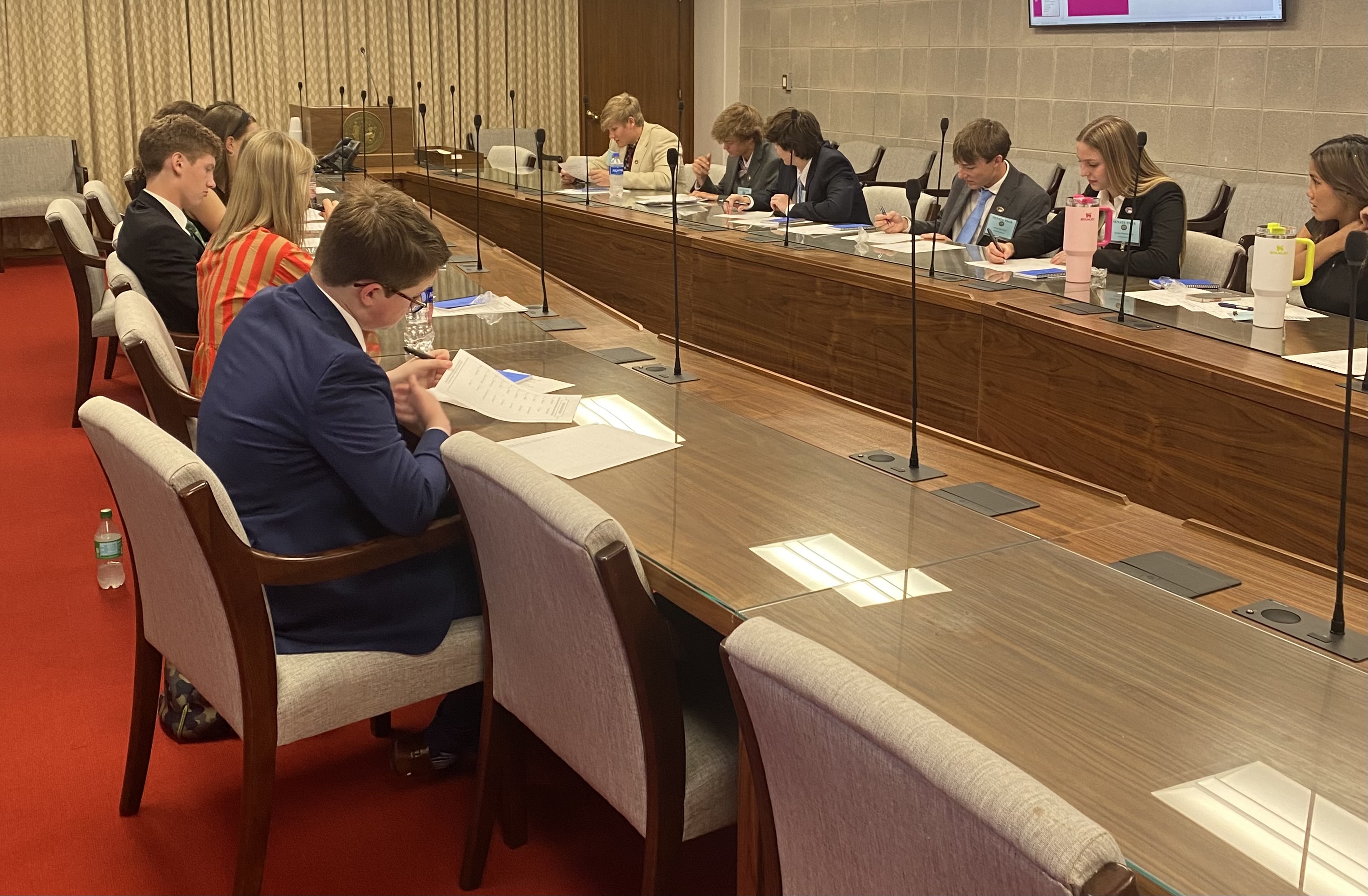 Pages seated at long table with microphones in committee room, looking at papers.